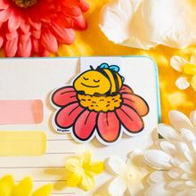 Load image into Gallery viewer, The Sleepy Bee Bamboo Sticker is an eco-friendly accessory featuring an adorable illustration of a drowsy bee. Crafted from 100% sustainable bamboo, this sticker measures approximately 3x3 inches. It is designed to be fade and weather-resistant, making it suitable for various surfaces such as hydro flasks, journals, and tote bags. The strong 3M water-resistant adhesive ensures durability and longevity. Due to the natural variations in bamboo, each sticker may have slight differences in color and appearance.