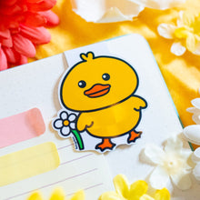 Load image into Gallery viewer, The "Duck with Flowers" magnetic bookmark is a charming and functional accessory for readers. It features a cute duck adorned with flowers, adding a touch of whimsy to your reading experience. The bookmark is double-sided, with a laminate on the front for protection and a glossy finish. Measuring approximately 2.4 inches on its longest side, it comes with a baby blue backing card. The strong magnets securely grip the pages of your book, ensuring you can easily return to where you left off
