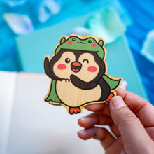 Load image into Gallery viewer, A quirky bamboo sticker featuring a penguin wearing a frog hat, looking cute and playful. This eco-friendly sticker has a fun, hand-drawn style, perfect for adding a touch of whimsy to your laptop, water bottle, or journal! 🐧🐸✨