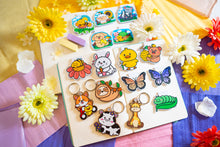Load image into Gallery viewer, A charming keychain featuring a cow surrounded by a cluster of delicate flowers. The cow has a sweet, cartoonish design with soft features and a peaceful expression, while the colorful flowers add a cheerful and whimsical touch. Made from durable material, this keychain is both cute and practical, perfect for decorating keys, bags, or backpacks