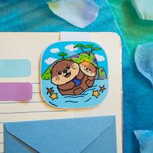 Load image into Gallery viewer, A delightful magnetic bookmark featuring a playful Monterey otter floating on its back, holding a seashell. This eco-friendly bookmark has a cute, hand-drawn style, perfect for adding a touch of ocean charm to your reading! 🦦🌊📖✨