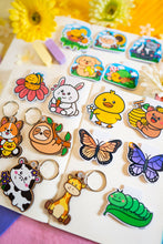 Load image into Gallery viewer, The Sleepy Hanging Sloth keychain is an eco-friendly accessory featuring an adorable illustration of a sloth hanging from a branch, appearing sleepy and content. Crafted from 100% sustainable bamboo, this sticker measures approximately 3x3 inches. It is designed to be fade and weather-resistant, making it suitable for various surfaces such as hydro flasks, journals, and tote bags. The strong 3M water-resistant adhesive ensures durability and longevity. Due to the natural variations in bamboo, each sti