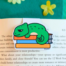 Load image into Gallery viewer, A vibrant magnetic bookmark featuring a charming chameleon design. The chameleon is illustrated in bright, playful colors with intricate details, such as a curled tail, textured scales, and a curious expression. Its body wraps seamlessly around the bookmark, making it both functional and eye-catching. The magnetic closure ensures it stays securely in place, adding a fun and whimsical touch to any book or planner. Perfect for animal lovers and book enthusiasts alike