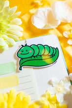 Load image into Gallery viewer, A charming magnetic bookmark featuring an adorable caterpillar design. The caterpillar is illustrated in a playful, cartoonish style with a series of bright, colorful segments and a happy, smiling face. Its whimsical details, like tiny antennae and cheerful eyes, make it a fun companion for any book. The fold-over magnetic closure keeps it securely in place, making it both practical and delightful for marking your pages. Perfect for book lovers and fans of cute critters!