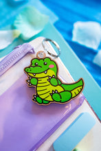 Load image into Gallery viewer, A bamboo keychain shaped like a crocodile, showcasing a detailed yet minimalist design. The crocodile features etched scales, a long snout, and a playful grin, all engraved into the natural bamboo material. The smooth wood grain adds a rustic and eco-friendly charm, while the compact size makes it perfect for keys, backpacks, or purses
