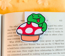 Load image into Gallery viewer, A whimsical magnetic bookmark featuring a cute frog sitting on a mushroom, surrounded by tiny details of nature. This eco-friendly bookmark has a charming, hand-drawn style, perfect for adding a touch of forest magic to your reading! 🐸🍄📖✨