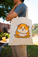 Load image into Gallery viewer, A cute and cuddly guinea pig sitting happily with a cheerful expression, surrounded by soft greenery. This eco-friendly tote bag features a playful, hand-drawn design, perfect for guinea pig lovers and everyday use! 🐹💚✨