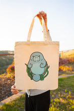Load image into Gallery viewer, A cute and lovable manatee floating happily in the water, surrounded by gentle waves. This eco-friendly tote bag features a soft, hand-drawn design, perfect for ocean lovers and everyday use. 🌊💙🐘💖