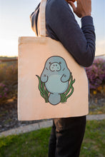 Load image into Gallery viewer, A cute and lovable manatee floating happily in the water, surrounded by gentle waves. This eco-friendly tote bag features a soft, hand-drawn design, perfect for ocean lovers and everyday use. 🌊💙🐘💖