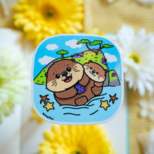 Load image into Gallery viewer, A glossy sticker featuring a cute otter with a playful expression. The otter is either floating on its back or holding a small object, giving off an adorable and cheerful vibe.
Let me know if you’d like any edits! 😊🦦✨