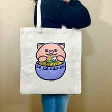 Load image into Gallery viewer, An adorable design featuring a happy pig enjoying a big bowl of ramen, complete with noodles, chopsticks, and tasty toppings! Printed on a durable, eco-friendly tote bag, perfect for carrying books, groceries, and daily essentials. A must-have for foodies and pig lovers alike!
