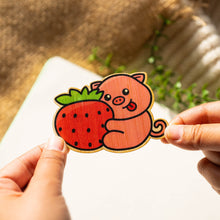 Load image into Gallery viewer, A cute pig happily hugging a big, juicy strawberry, with a soft pastel background. This eco-friendly bamboo sticker has an adorable, hand-drawn style, perfect for decorating laptops, water bottles, and notebooks. 🍓🐷💖