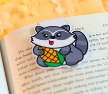 Load image into Gallery viewer, A fun magnetic bookmark featuring a mischievous raccoon holding a piece of corn with a cheeky grin. This eco-friendly bookmark has a playful, hand-drawn style, perfect for adding a touch of whimsy to your reading! 🦝🌽📖✨