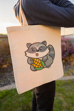 Load image into Gallery viewer, A playful design featuring a mischievous raccoon happily munching on a fresh ear of corn! Printed on a durable, eco-friendly tote bag, perfect for carrying books, groceries, or everyday essentials. A fun and quirky choice for raccoon lovers and foodies!