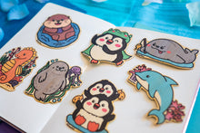 Load image into Gallery viewer, A cute sea otter floating happily on its back, holding a seashell with a cheerful expression. This eco-friendly bamboo sticker features a charming, hand-drawn style, perfect for decorating laptops, water bottles, and journals! 🦦💙✨