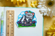 Load image into Gallery viewer, A glossy sticker featuring a cute black-and-white skunk with a fluffy tail and a tiny gray mouse sitting beside it. The two animals appear friendly and curious, creating a charming and heartwarming design.