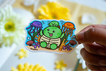 Load image into Gallery viewer, A glossy sticker depicting a mother and baby turtle swimming among jellyfish and coral reefs. Available at Modern Mous