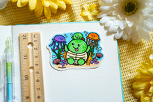 Load image into Gallery viewer, A glossy sticker depicting a mother and baby turtle swimming among jellyfish and coral reefs. Available at Modern Mous