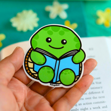 Load image into Gallery viewer, A glossy sticker featuring a turtle reading a book, available on Redbubble