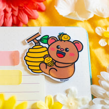 Load image into Gallery viewer, A cute bookmark featuring a bear with a bee buzzing around it, and a detailed beehive in the background. The design is playful and charming, perfect for marking your place in a book