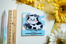 Load image into Gallery viewer, A magnetic bookmark featuring a delightful design of cows and flowers. The cows are illustrated in a cute, cartoonish style, surrounded by vibrant flowers in various shapes and colors. The fold-over magnetic closure ensures it stays securely on your page, while the cheerful design adds a touch of whimsy to any book or planner. Perfect for animal lovers and avid readers alike