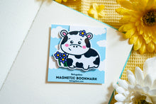 Load image into Gallery viewer, A magnetic bookmark featuring a delightful design of cows and flowers. The cows are illustrated in a cute, cartoonish style, surrounded by vibrant flowers in various shapes and colors. The fold-over magnetic closure ensures it stays securely on your page, while the cheerful design adds a touch of whimsy to any book or planner. Perfect for animal lovers and avid readers alike
