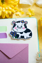 Load image into Gallery viewer, A magnetic bookmark featuring a delightful design of cows and flowers. The cows are illustrated in a cute, cartoonish style, surrounded by vibrant flowers in various shapes and colors. The fold-over magnetic closure ensures it stays securely on your page, while the cheerful design adds a touch of whimsy to any book or planner. Perfect for animal lovers and avid readers alike