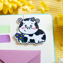 Load image into Gallery viewer, A magnetic bookmark featuring a delightful design of cows and flowers. The cows are illustrated in a cute, cartoonish style, surrounded by vibrant flowers in various shapes and colors. The fold-over magnetic closure ensures it stays securely on your page, while the cheerful design adds a touch of whimsy to any book or planner. Perfect for animal lovers and avid readers alike
