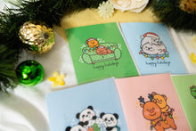 Load image into Gallery viewer, A delightful set of holiday greeting cards featuring whimsical, festive designs. Each card showcases unique artwork, including a cheerful snowman with a cozy scarf, a Christmas tree adorned with colorful ornaments, a playful reindeer with twinkling lights tangled in its antlers, and a warm fireplace scene with stockings hung with care. The cards are accented with gold foil details, vibrant colors, and charming holiday-themed illustrations, perfect for spreading joy and festive cheer to family and friends.