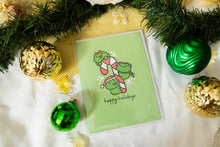 Load image into Gallery viewer, A delightful set of holiday greeting cards featuring whimsical, festive designs. Each card showcases unique artwork, including a cheerful snowman with a cozy scarf, a Christmas tree adorned with colorful ornaments, a playful reindeer with twinkling lights tangled in its antlers, and a warm fireplace scene with stockings hung with care. The cards are accented with gold foil details, vibrant colors, and charming holiday-themed illustrations, perfect for spreading joy and festive cheer to family and friends.