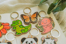 Load image into Gallery viewer, A bamboo keychain shaped like a crocodile, showcasing a detailed yet minimalist design. The crocodile features etched scales, a long snout, and a playful grin, all engraved into the natural bamboo material. The smooth wood grain adds a rustic and eco-friendly charm, while the compact size makes it perfect for keys, backpacks, or purses