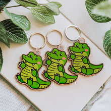Load image into Gallery viewer, A bamboo keychain shaped like a crocodile, showcasing a detailed yet minimalist design. The crocodile features etched scales, a long snout, and a playful grin, all engraved into the natural bamboo material. The smooth wood grain adds a rustic and eco-friendly charm, while the compact size makes it perfect for keys, backpacks, or purses
