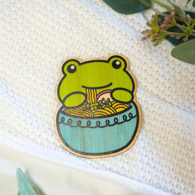 Belugabee Bamboo Sticker: Adorable frog slurping noodles from a blue ramen bowl, crafted on eco-friendly bamboo. Elevate your style with this charming 3x3-inch sticker. 🐸🍜 #BambooSticker #FrogRamen #HumorousDesign