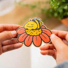 Load image into Gallery viewer, A cozy, sleepy bee curled up with tiny "Zzz" floating above, resting on a fluffy flower. This eco-friendly bamboo sticker has a soft, hand-drawn style, perfect for adding a touch of charm to laptops, water bottles, and journals