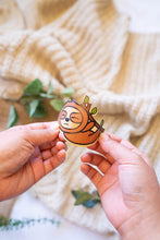 Load image into Gallery viewer, The Sleepy Hanging Sloth Bamboo Sticker is an eco-friendly accessory featuring an adorable illustration of a sloth hanging from a branch, appearing sleepy and content. Crafted from 100% sustainable bamboo, this sticker measures approximately 3x3 inches. It is designed to be fade and weather-resistant, making it suitable for various surfaces such as hydro flasks, journals, and tote bags. The strong 3M water-resistant adhesive ensures durability and longevity. Due to the natural variations in bamboo, each sti