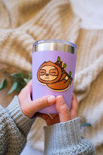 Load image into Gallery viewer, The Sleepy Hanging Sloth Bamboo Sticker is an eco-friendly accessory featuring an adorable illustration of a sloth hanging from a branch, appearing sleepy and content. Crafted from 100% sustainable bamboo, this sticker measures approximately 3x3 inches. It is designed to be fade and weather-resistant, making it suitable for various surfaces such as hydro flasks, journals, and tote bags. The strong 3M water-resistant adhesive ensures durability and longevity. Due to the natural variations in bamboo, each sti