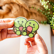 Load image into Gallery viewer, A cute turtle with a happy expression, carrying a delicious dessert on its shell! This eco-friendly bamboo sticker features vibrant colors and charming details, perfect for decorating water bottles, laptops, and notebooks. A sweet treat for turtle lovers and dessert enthusiasts alike!