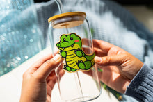 Load image into Gallery viewer, Belugabee Bamboo Sticker: Striking green crocodile design adorning a glass cup, infusing wild charm into your drinkware. Elevate your style with this eco-friendly 3x3-inch bamboo sticker. 🐊🌿 #BambooSticker #GreenCrocodile #GlassCupDecor