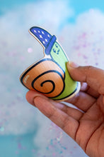 Load image into Gallery viewer, The Wizard Snail Bamboo Sticker is an eco-friendly decorative item featuring a whimsical illustration of a snail adorned with wizard attire. Crafted from 100% sustainable bamboo, this sticker measures approximately 3x3 inches and is designed to be both fade and weather-resistant. Its strong 3M water-resistant adhesive ensures durability across various surfaces, including hydro flasks, journals, and tote bags. This sticker combines environmental consciousness with a touch of fantasy, making it a delightful a