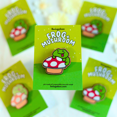 A whimsical wooden pin featuring a cute frog sitting on a mushroom, surrounded by tiny natural details. This eco-friendly pin has a charming, hand-carved design, perfect for adding a touch of nature-inspired magic to your bag or jacket! 🐸🍄✨