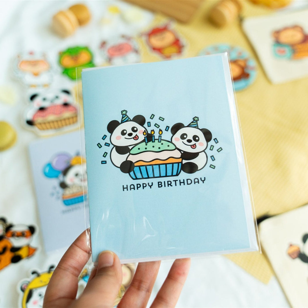 A charming birthday card featuring adorable pandas, each with a joyful expression, surrounding a delicious-looking cupcake topped with colorful frosting and a candle. The card includes the message 