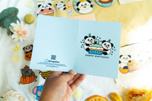 Load image into Gallery viewer, A charming birthday card featuring adorable pandas, each with a joyful expression, surrounding a delicious-looking cupcake topped with colorful frosting and a candle. The card includes the message &quot;Happy Birthday&quot; in playful, vibrant lettering, adding a festive touch to the celebration
