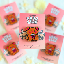 Load image into Gallery viewer, A wooden pin shaped like a bear holding a cup of boba tea. The bear has a cute, cartoonish design with rounded features and a friendly expression. The cup of boba tea is detailed with tiny tapioca pearls at the bottom, and the bear appears to be happily sipping through a straw. The wood has a natural grain, adding a rustic charm to the design
