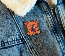 Load image into Gallery viewer, A wooden pin shaped like a bear holding a cup of boba tea. The bear has a cute, cartoonish design with rounded features and a friendly expression. The cup of boba tea is detailed with tiny tapioca pearls at the bottom, and the bear appears to be happily sipping through a straw. The wood has a natural grain, adding a rustic charm to the design
