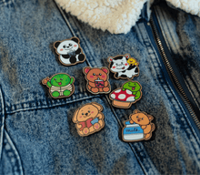 Load image into Gallery viewer, 
A vibrant collection of wooden pins featuring adorable animal designs. The set includes a cheerful turtle with a bright shell, a cute cow with soft spots, a happy ducky with a tiny beak, and a playful frog mid-hop. There’s also a boba bear and boba panda, each holding a cup of boba tea with tapioca pearls, a reading panda (“Pu”) engrossed in a book, and a hungry kitty with a charmingly mischievous expression. Each pin is detailed with colorful accents and natural wood grain, adding personality and whimsy t
