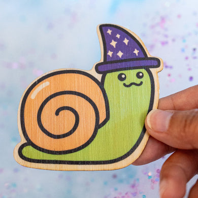 The Wizard Snail Bamboo Sticker is an eco-friendly decorative item featuring a whimsical illustration of a snail adorned with wizard attire. Crafted from 100% sustainable bamboo, this sticker measures approximately 3x3 inches and is designed to be both fade and weather-resistant. Its strong 3M water-resistant adhesive ensures durability across various surfaces, including hydro flasks, journals, and tote bags. This sticker combines environmental consciousness with a touch of fantasy, making it a delightful a