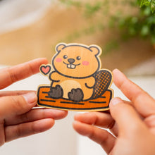 Load image into Gallery viewer, Bamboo Sticker of a Beaver on a log with a cute heart, Brown Beaver sitting on brown wood log holding up a red heart on right hand 
