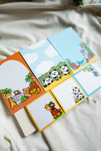 Load image into Gallery viewer,  Zoo animals come to life on the large orange memo pad with palm trees, featuring a playful cast including a giraffe, elephant, monkey, turtle, lion, and bear. On the blue and white panda memo pad, adorable pandas play among bamboo sticks in a cloud-filled backdrop. Dive into the ocean with the aquatic-themed memo pad showcasing the ocean floor, complete with a stingray, corals, and jellyfish. Below, find smaller versions of each design in the form of convenient sticky notes.
